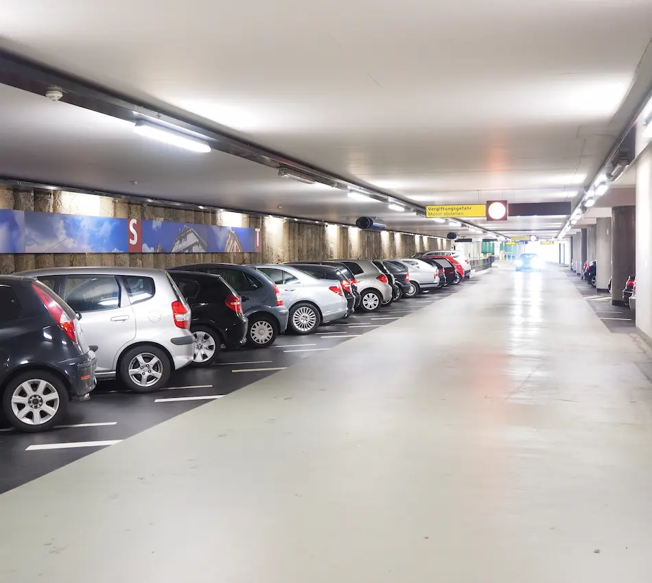 Estacionamiento subterráneo con varios coches alineados a la izquierda y señalización en el fondo.