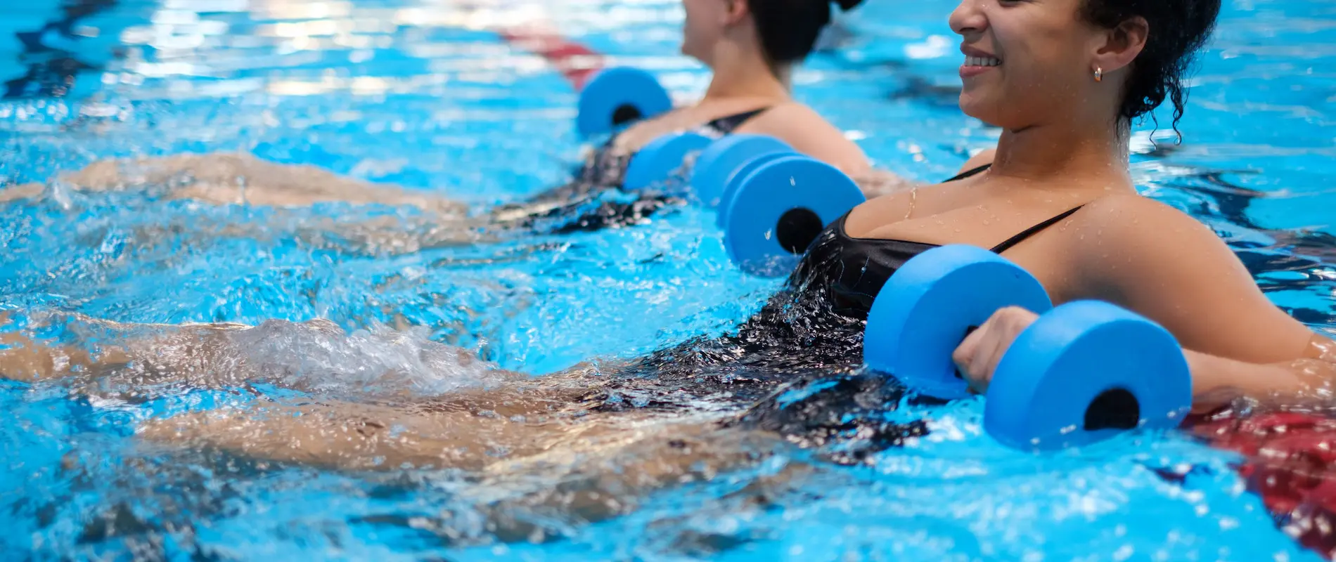 Mujeres haciendo ejercicios acuáticos con pesas en una piscina.