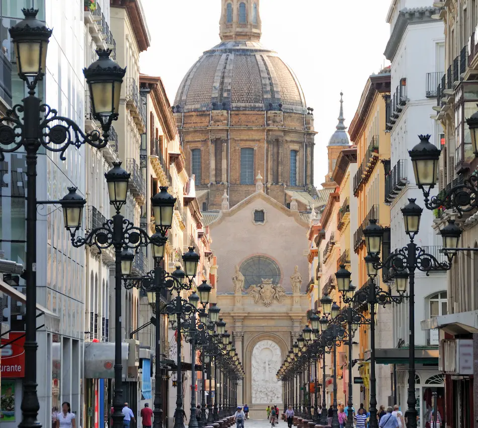 Calle con faroles y edificios, al fondo una iglesia con gran cúpula.
