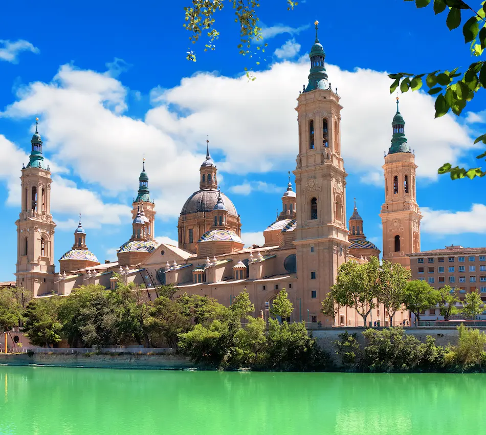 Gran iglesia de cúpulas y torres junto a un río verde, cielo azul y nubes.