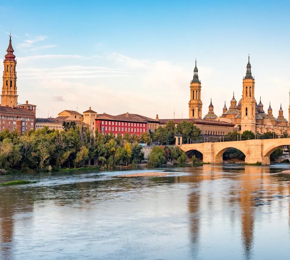 Una catedral y un puente reflejados en un río al atardecer.