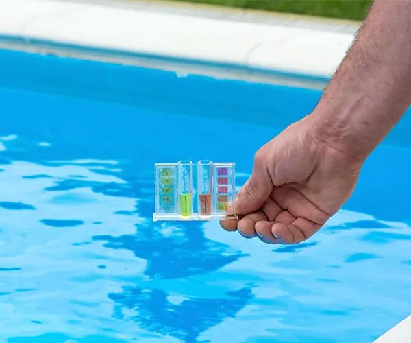 Mano sosteniendo kit de prueba química sobre agua de piscina.