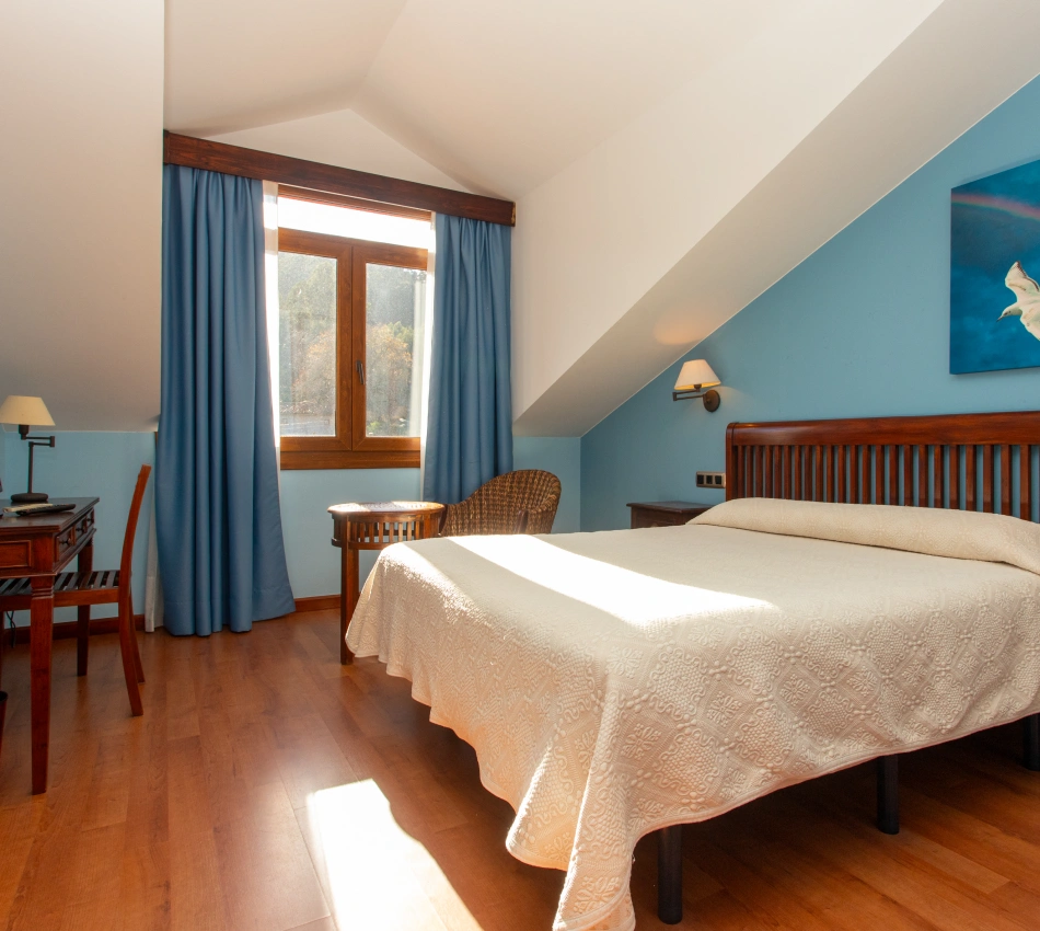 Habitaci&oacute;n con cama, muebles de madera, cortinas azules, y luz natural entrando por una ventana.