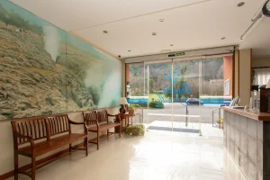 Lobby de hotel con bancas de madera, mural rocoso y puerta de vidrio con vista al exterior.