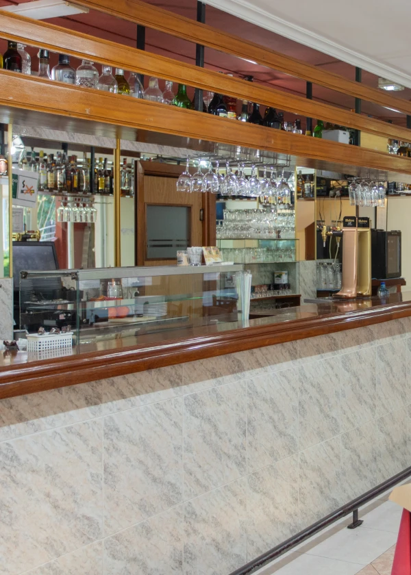 Bar con estante de botellas, copas colgadas y barra de m&aacute;rmol beige con madera pulida.