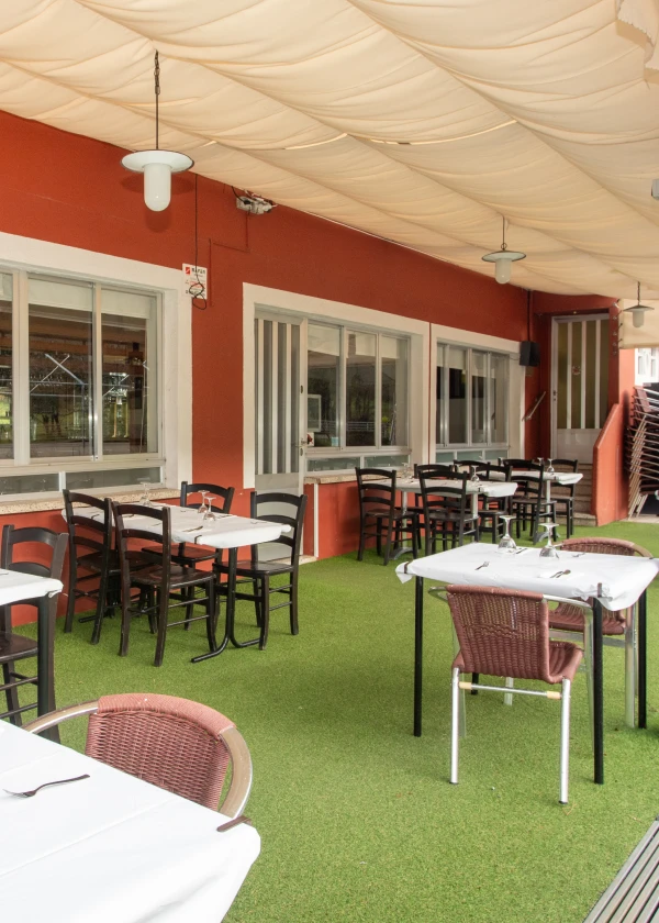 Terraza de restaurante con mesas y sillas sobre c&eacute;sped artificial y techo cubierto.