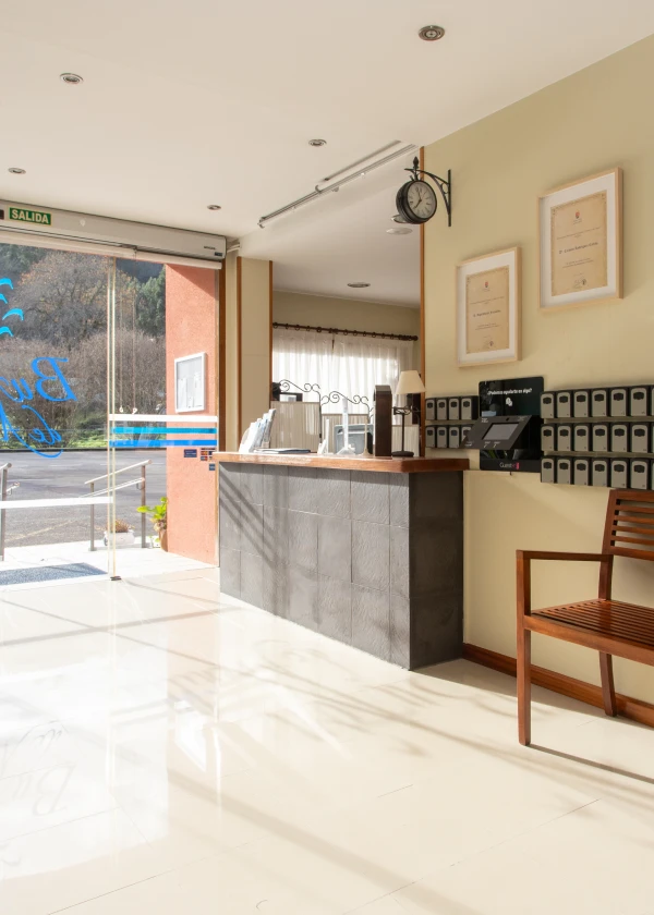 Recepci&oacute;n de hotel con escritorio, silla, cuadros y puerta de vidrio que da al exterior.
