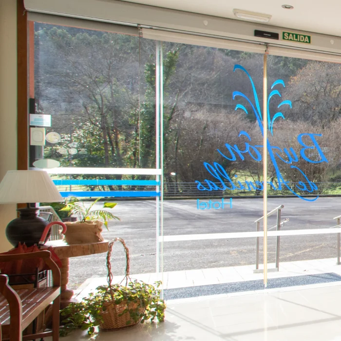 Entrada de un hotel con puerta de vidrio, plantas decorativas y letrero azul en la puerta.