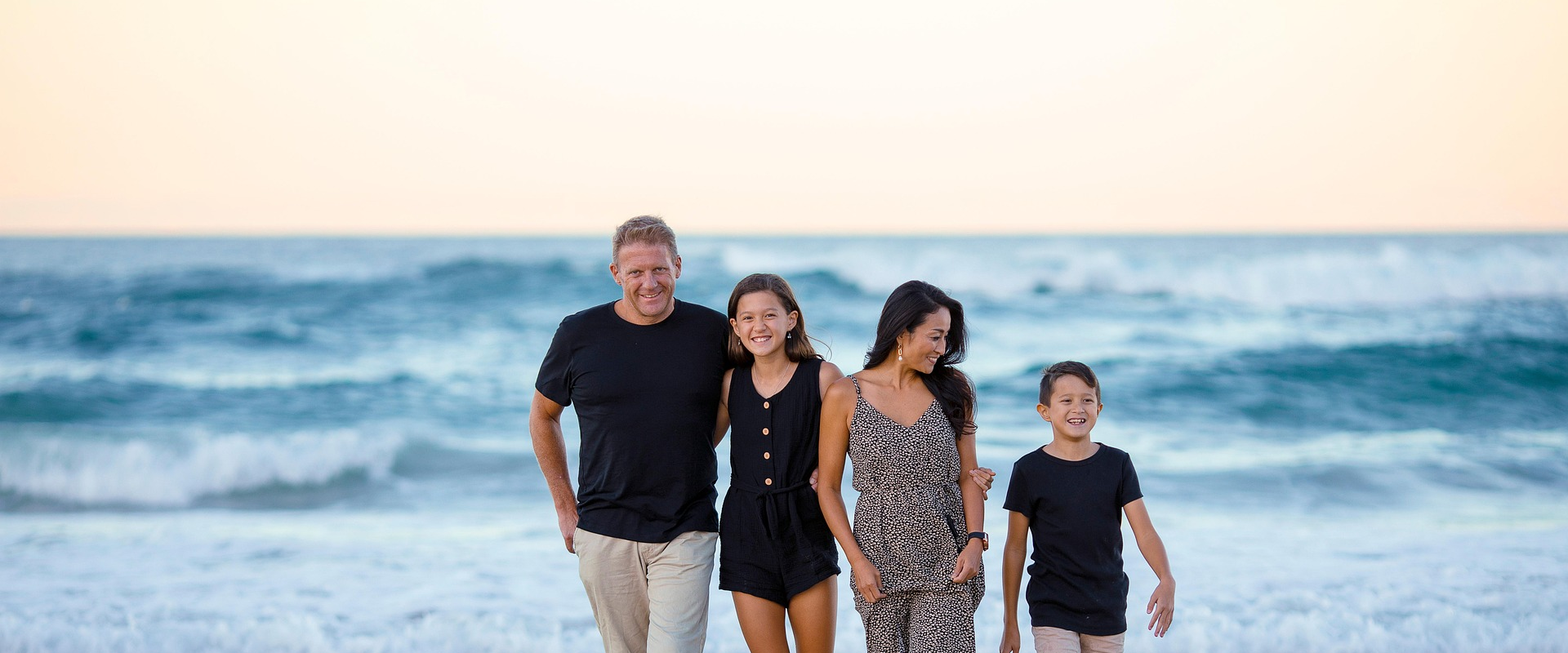 Familia caminando en la playa al atardecer, con el mar de fondo y sonrisas en sus rostros.