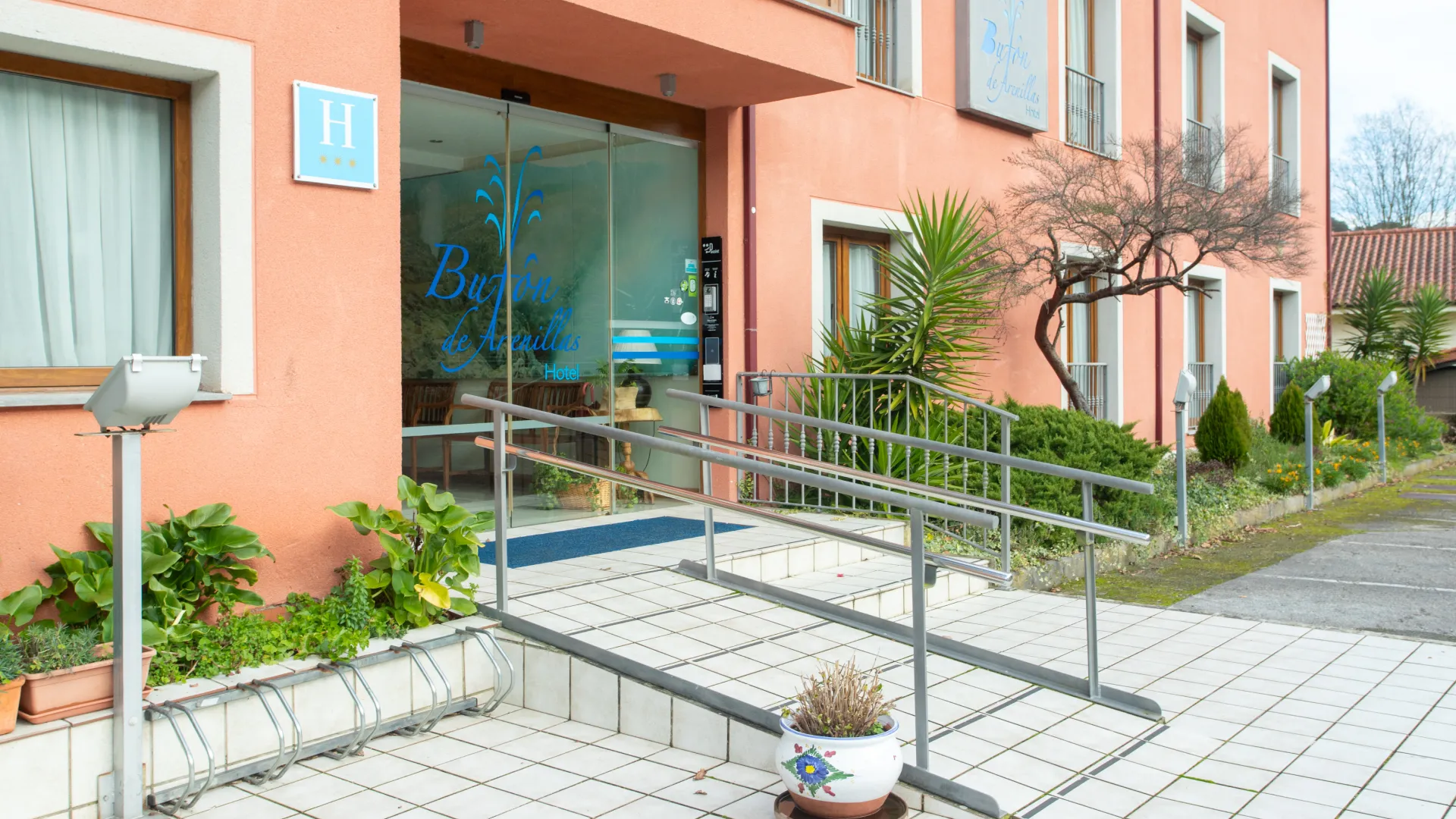 Entrada de hotel color salm&oacute;n con rampa accesible y plantas decorativas.
