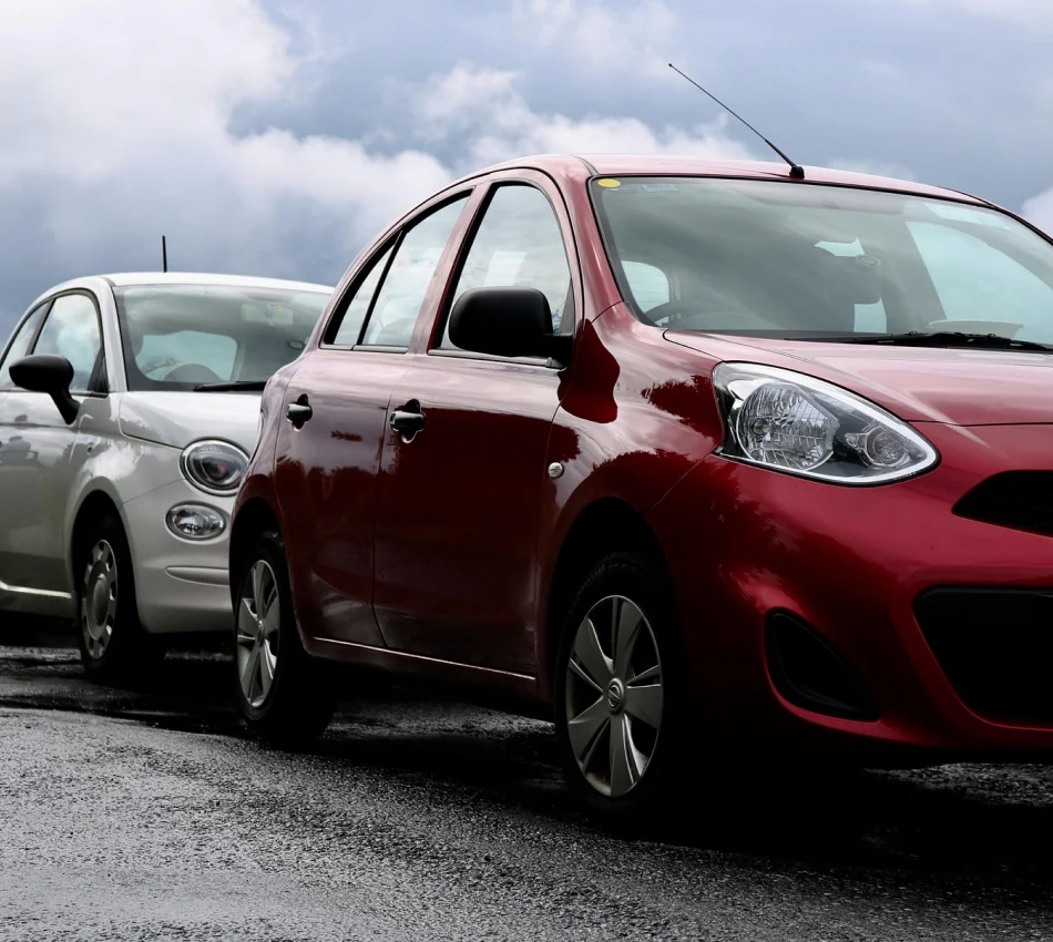 Dos autom&oacute;viles estacionados, uno rojo y otro blanco, bajo un cielo nublado.