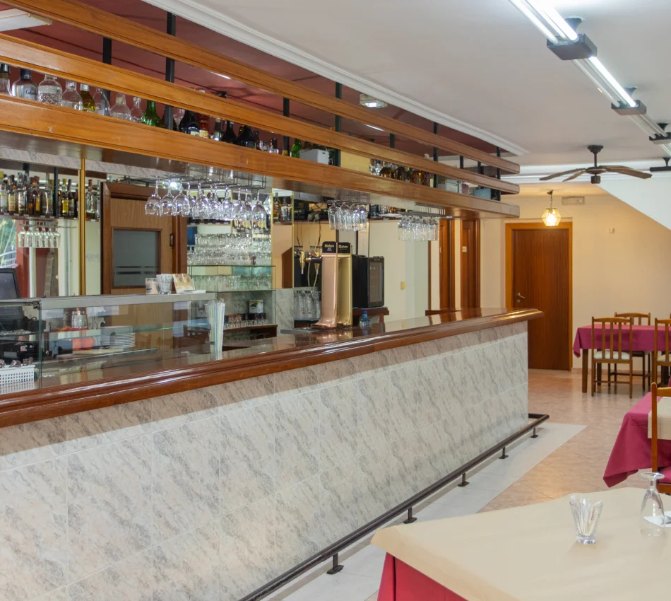 Bar con barra de m&aacute;rmol, copas colgantes y mesas con manteles rojos.