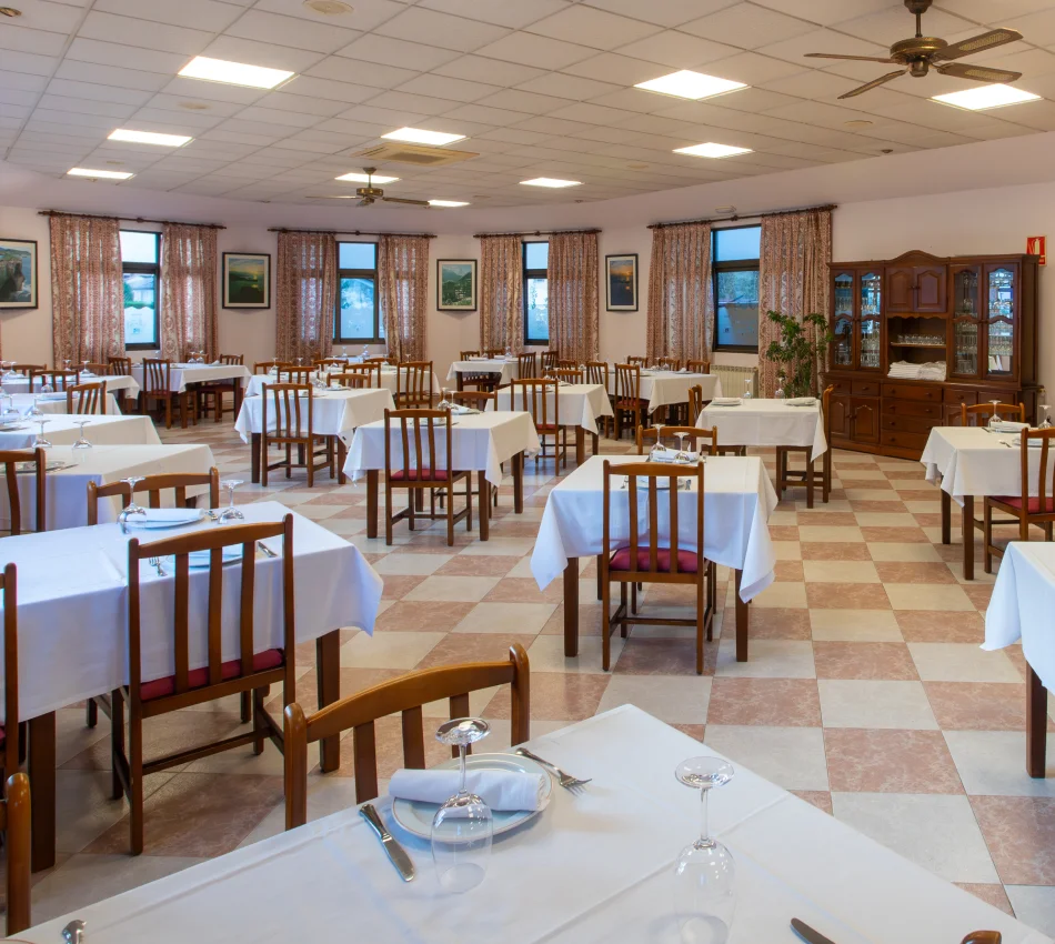Un comedor amplio con mesas bien dispuestas y cubiertos listos, en un ambiente acogedor.