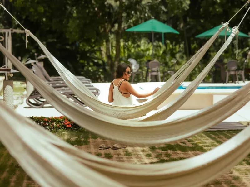 Mujer sentada en tumbona de jardín, rodeada de hamacas y sombrillas verdes.