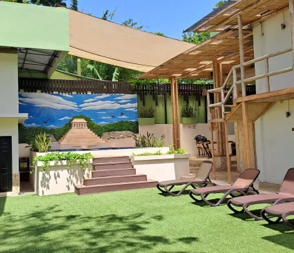 &Aacute;rea al aire libre con sillas, pintura de pir&aacute;mide, &aacute;rboles y estructuras de madera y metal.