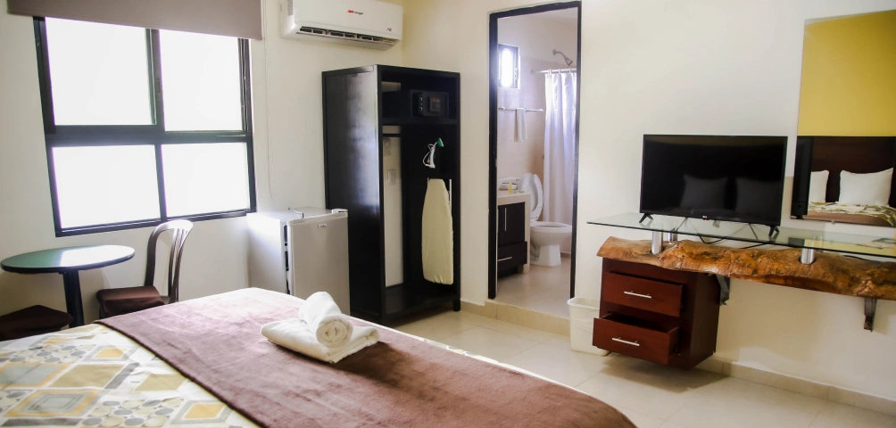 Habitaci&oacute;n de hotel moderna con cama, televisor, ba&ntilde;o privado y ventanas grandes.