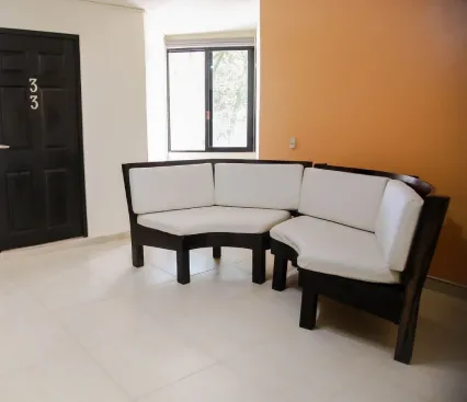 Sala de espera con sof&aacute; esquinero, pared naranja y puerta negra con n&uacute;mero 33.