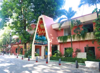 Edificio rosado con mural de sol, rodeado de &aacute;rboles y jardines.