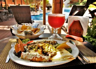 Plato de comida mexicana con bebida roja junto a una piscina en un ambiente al aire libre.