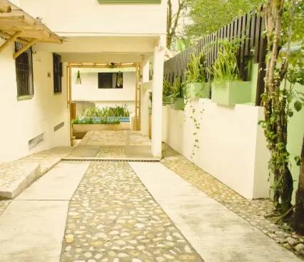 Pasillo exterior con suelo de piedras, plantas en los muros y un techo de madera.