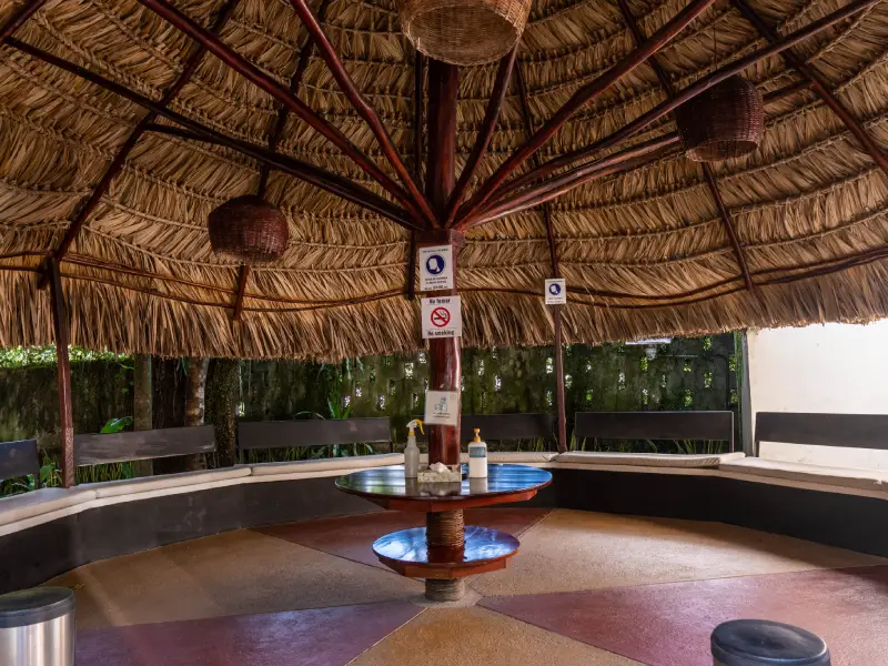 Interior de un quiosco con techo de paja, bancos circulares y mesa central con productos.