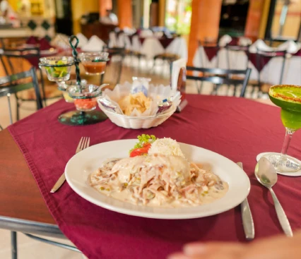 Plato de pasta en salsa blanca en un restaurante con mesas cubiertas de manteles burdeos.