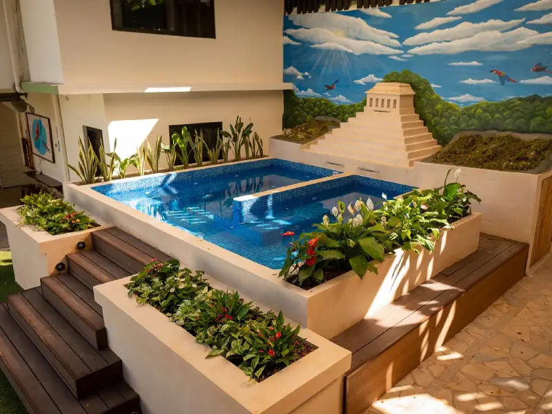 Piscina rodeada de plantas, con mural de pir&aacute;mide y paisaje natural en la pared.