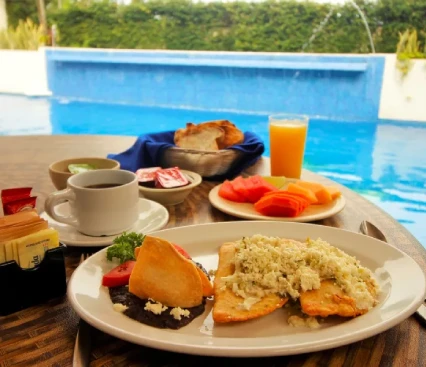 Desayuno junto a la piscina con chilaquiles, fruta, caf&eacute; y jugo de naranja en una mesa de madera.