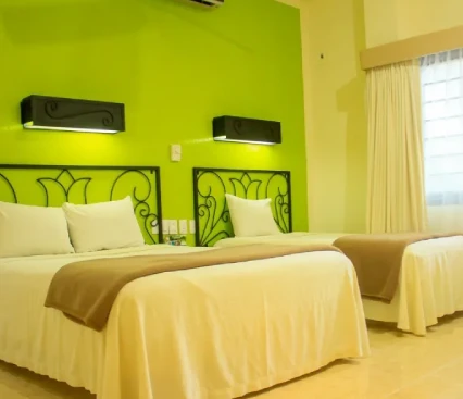 Habitaci&oacute;n de hotel con dos camas, paredes verdes y l&aacute;mparas de pared elegantes.