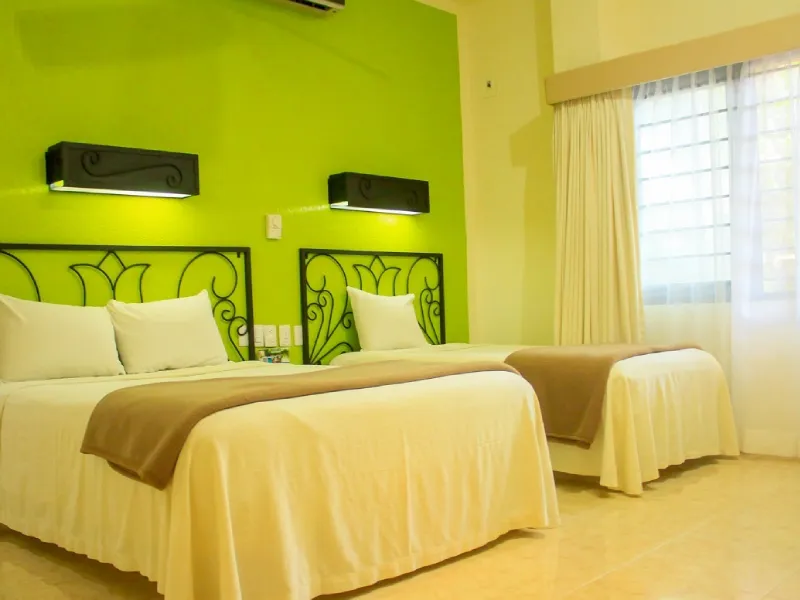 Habitaci&oacute;n con dos camas, fondo verde, cabeceras marrones y ventana con cortinas blancas.