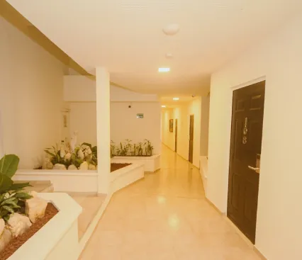 Pasillo interior con plantas y puertas en una pared blanca.