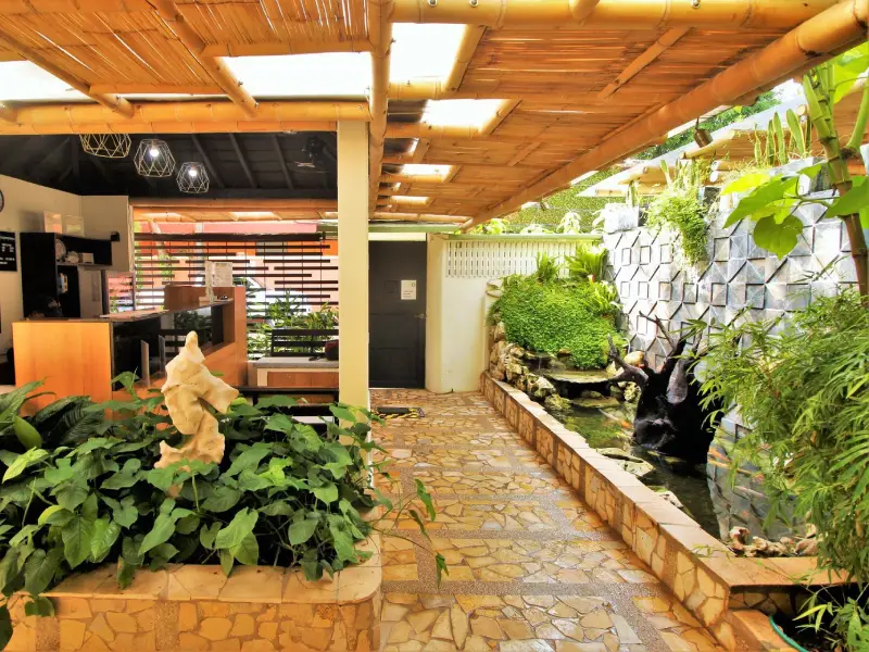 Espacio interior con jard&iacute;n, techo de bamb&uacute; y estanque rodeado de plantas y esculturas.