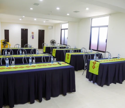 Sala de conferencias con mesas y sillas, botellas de agua y decoraci&oacute;n colorida sobre las mesas.