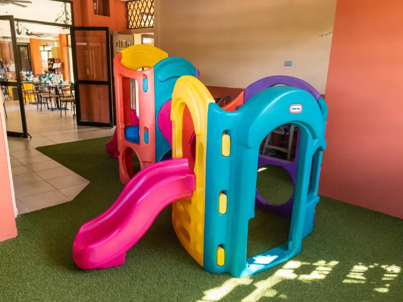 Estructura de juego infantil colorida con tobogán en área interior con césped artificial.