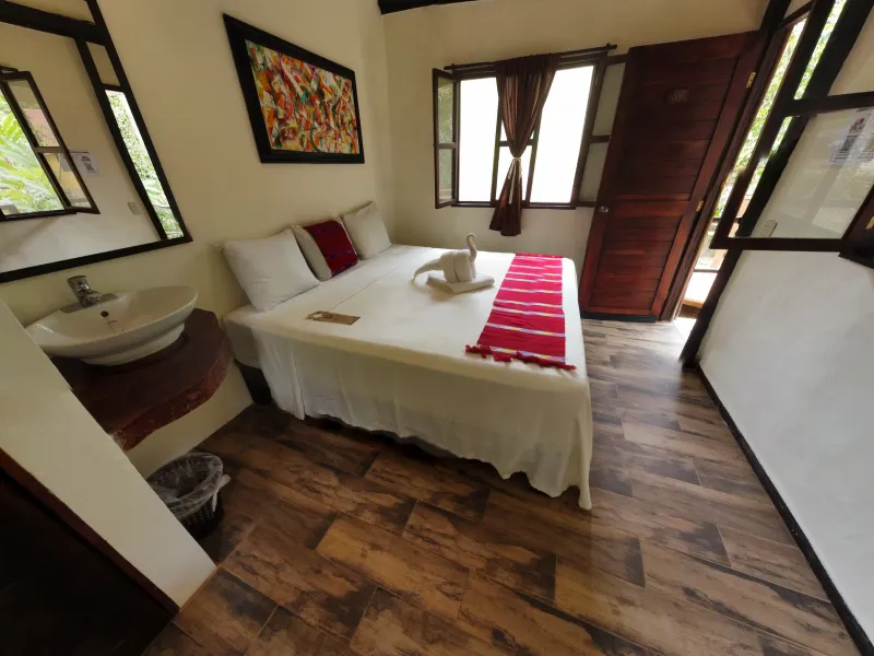 Habitación con cama doble, decorada con un cisne de toalla, ventanas y lavabo al fondo.