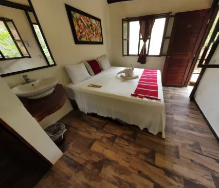 Habitaci&oacute;n con cama doble, decoraci&oacute;n colorida, lavabo y ventanas con cortinas.