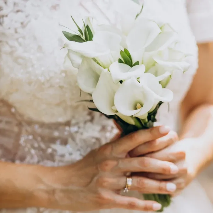 Manos sosteniendo un ramo de flores blancas, vistiendo un vestido de encaje.
