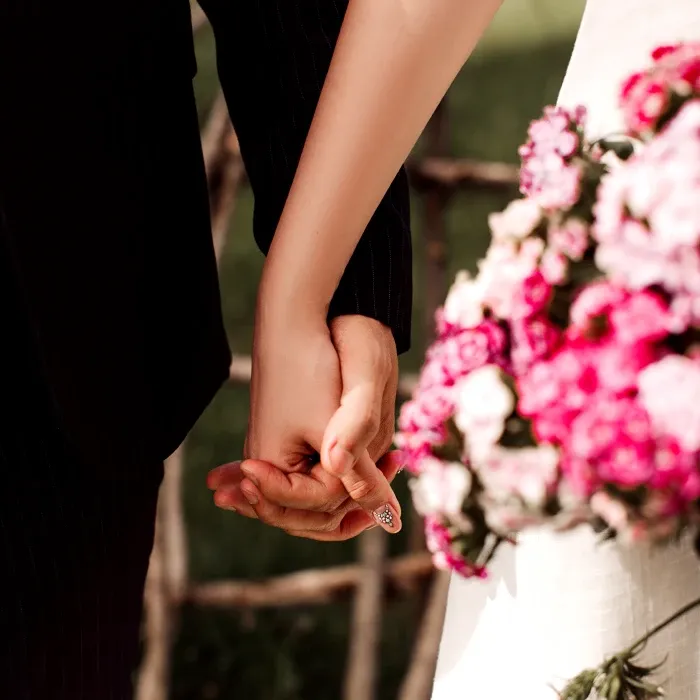 Pareja tomados de la mano, con ramo de flores rosas y fondo natural.