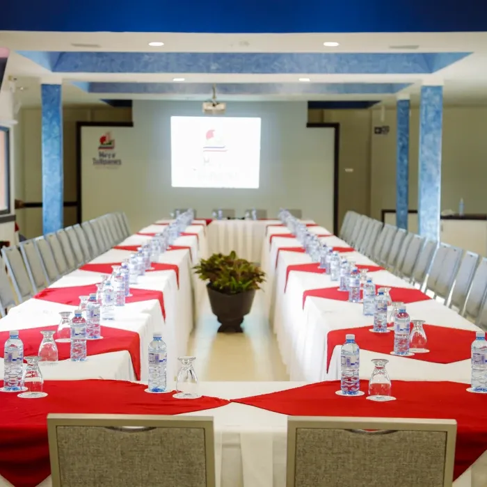 Mesa de conferencia en forma de U, con manteles rojos, vasos y botellas de agua.