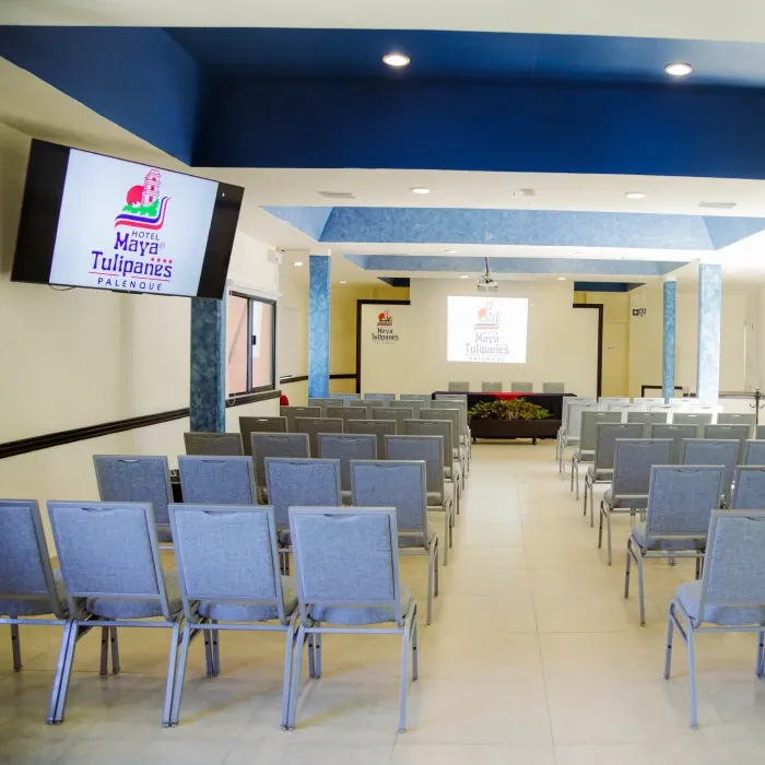 Sala de conferencias del Hotel Maya Tulipanes con sillas organizadas y pantallas al frente.
