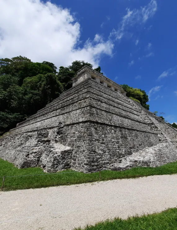 Pir&aacute;mide de piedra escalonada bajo un cielo azul y rodeada de vegetaci&oacute;n.