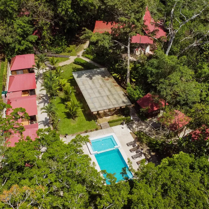 Vista a&eacute;rea de caba&ntilde;as rojas con piscina, rodeadas de &aacute;rboles y senderos en un entorno natural.