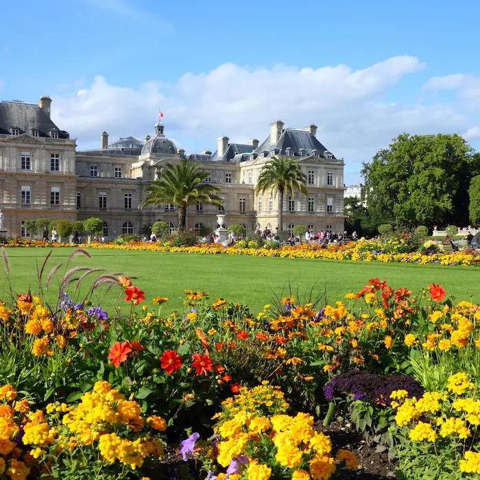 Jardin fleuri devant un grand bâtiment historique sous un ciel bleu.