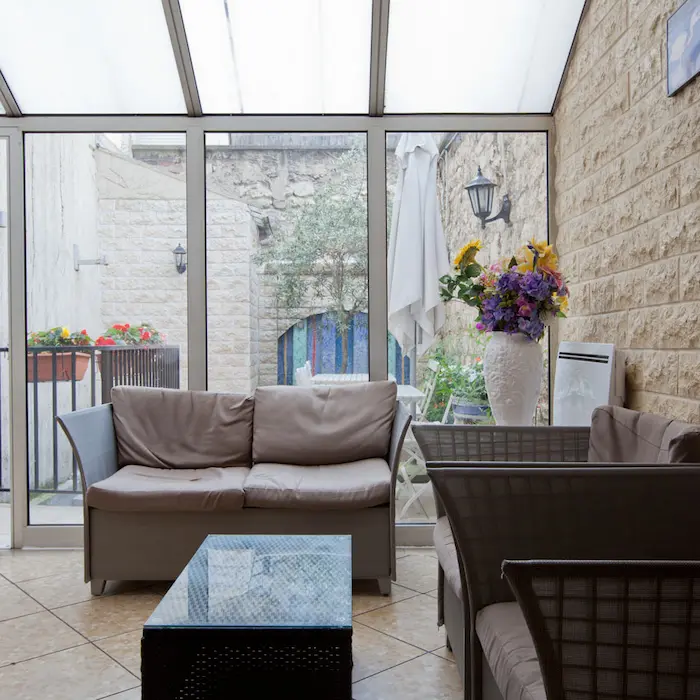 Canapé et fauteuils dans une véranda lumineuse, décorés de fleurs avec vue sur le patio en pierre.