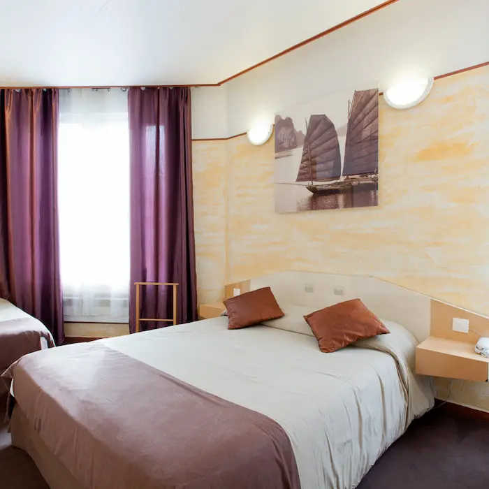 Chambre d'hôtel avec grand lit, rideaux violets et tableau de bateau sur le mur.