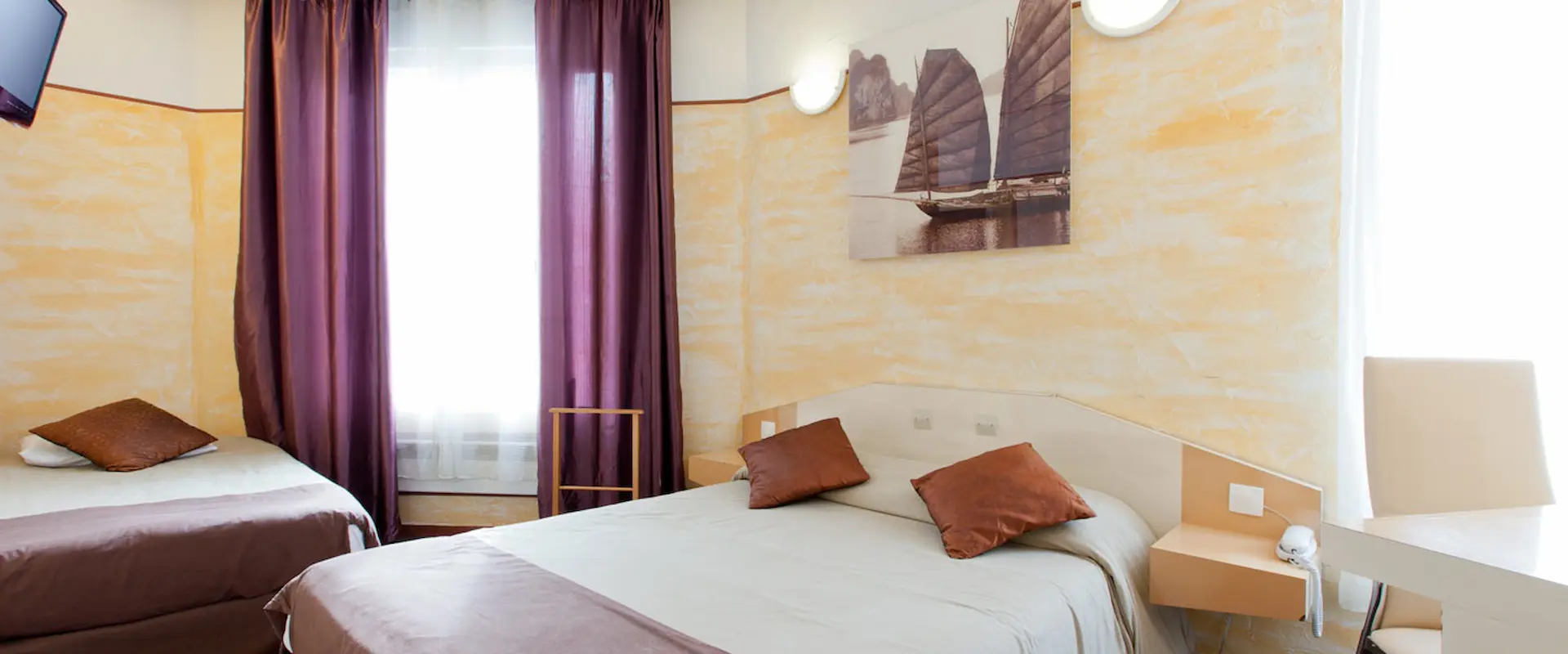 Chambre d'hôtel avec lits, rideaux violets et tableau de bateaux.