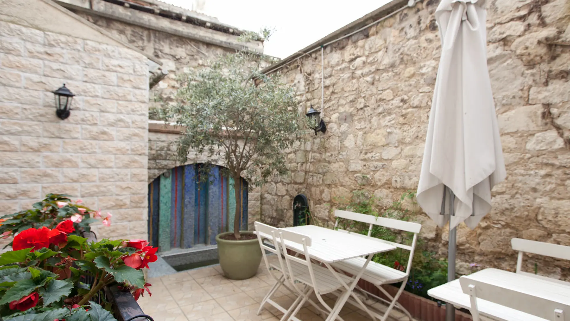 Terrasse en pierre avec table blanche, chaises, fleurs rouges, et un arbre en pot.
