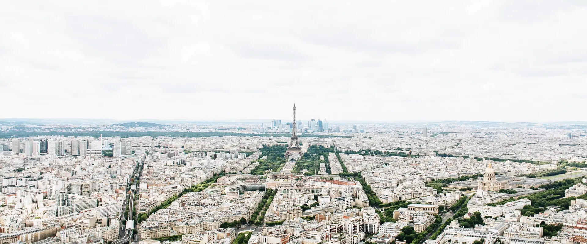 Vue panoramique de Paris avec la tour Eiffel au centre sous un ciel nuageux.