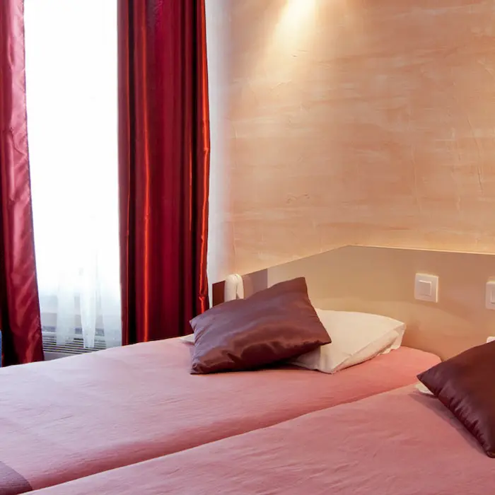 Deux lits simples avec coussins marron dans une chambre à éclairage doux.