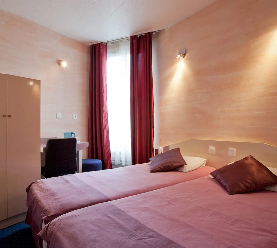 Chambre d'hôtel avec lits jumeaux, rideaux rouges et bureau.